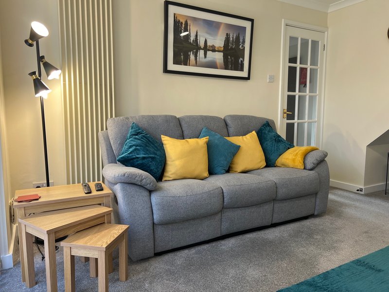 Living room with grey upholstered sofa, yellow and teal cushions, wooden nesting tables, floor lamp