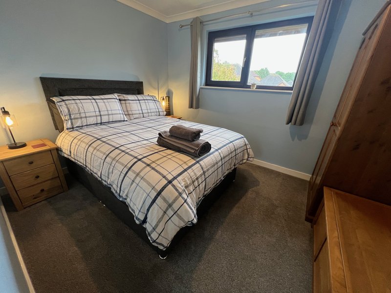 Bedroom with double bed, plaid bedding, wooden nightstand, and window with natural light