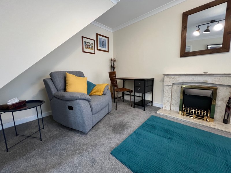 Attic living room with gray recliner, fireplace, desk, and teal area rug