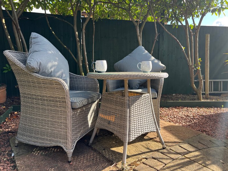 Outdoor seating area with wicker armchair, small table, cushions and trees