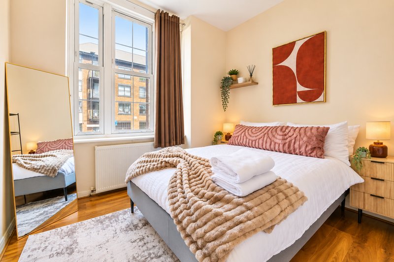 Bright bedroom with double bed, wooden floor, mirror, window with city view