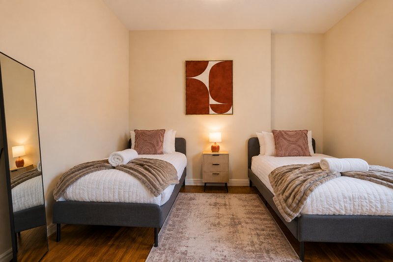 Twin bedroom with two single beds, bedside lamps, wall art, and wooden flooring