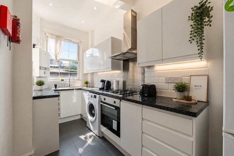 Modern white kitchen with black worktops, integrated appliances, and window overlooking garden