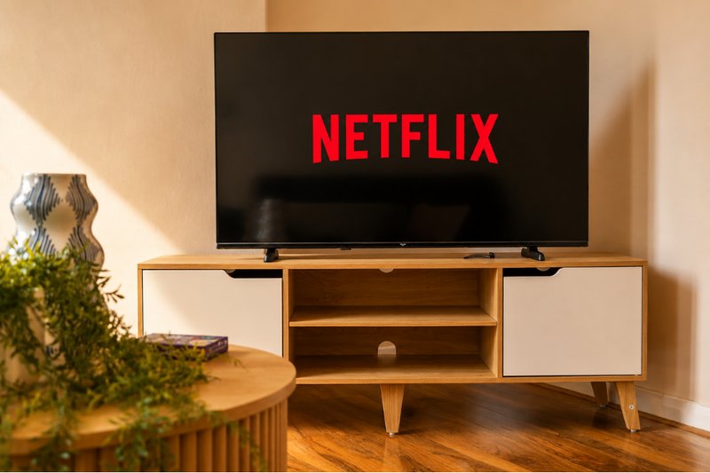 Living room with wooden TV stand, flat-screen television, and potted plant on side table