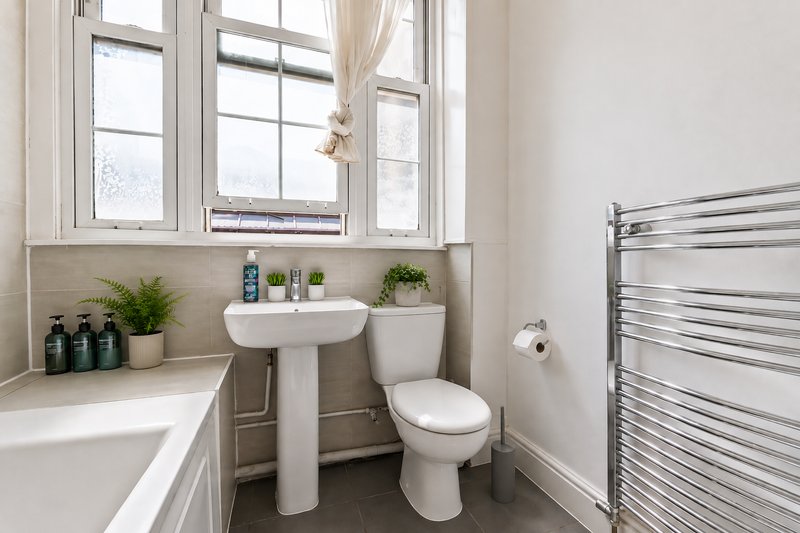 Clean modern bathroom with pedestal sink, toilet, heated towel rail and large window