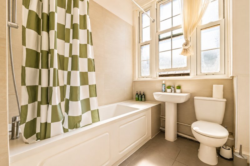 Bathroom with bathtub, pedestal sink, toilet, checkered shower curtain and window