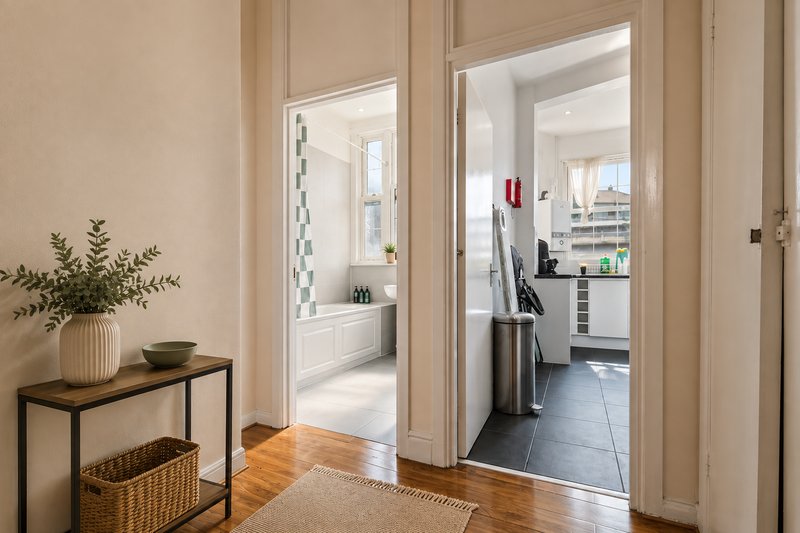 Modern entryway with wooden floor, console table with plants, and open doorways to kitchen and bathroom