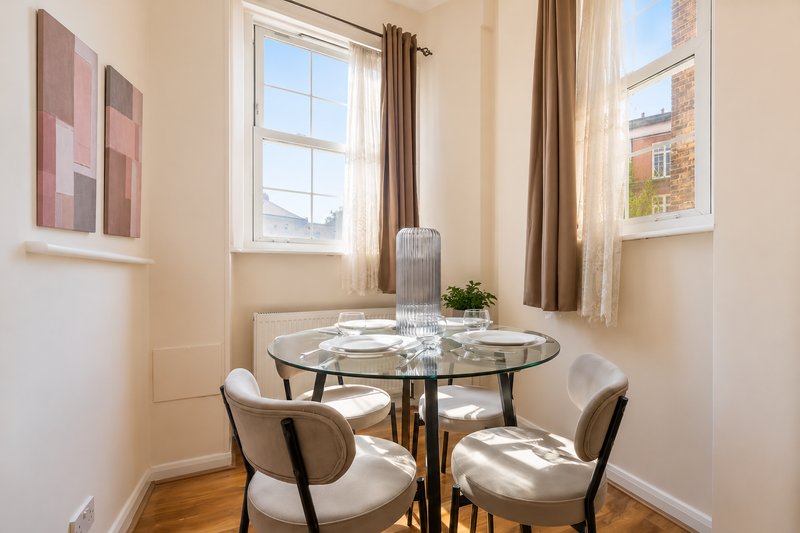 Bright dining nook with round glass table, two cream chairs, and large windows with city views