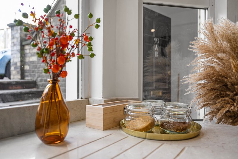 Modern windowsill with amber vase, flowers, dried pampas grass, and glass storage jars