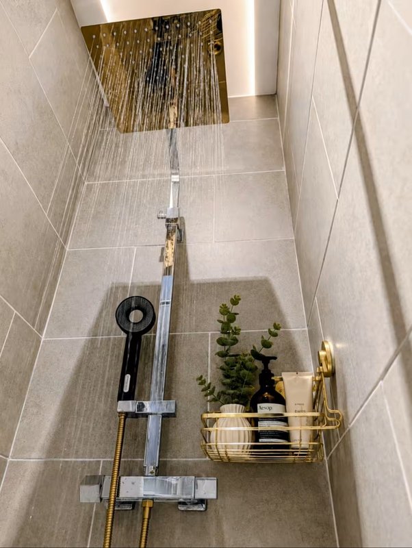 Modern bathroom shower area with gold rainfall showerhead, black hand shower, potted plant and accessories