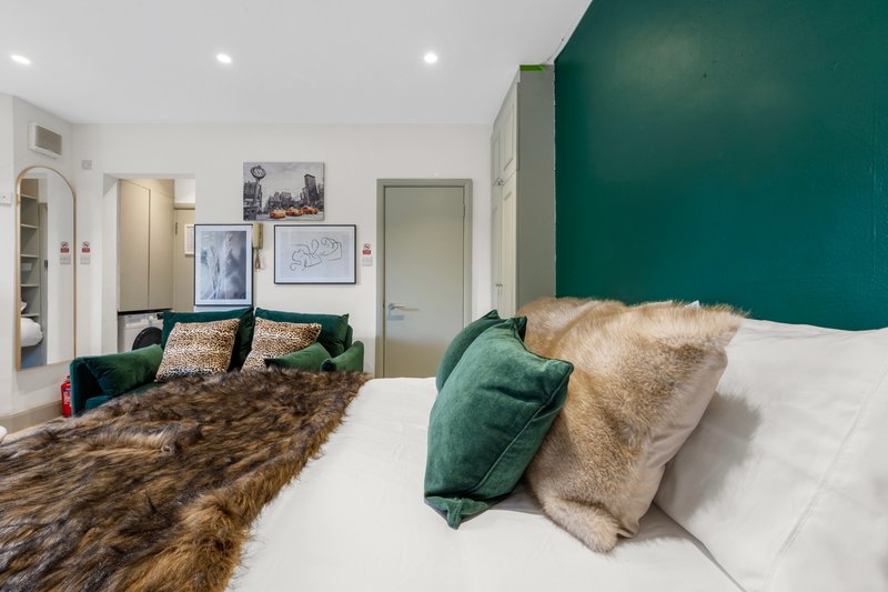 Modern bedroom with green accent wall, double bed, faux fur throws and decorative cushions