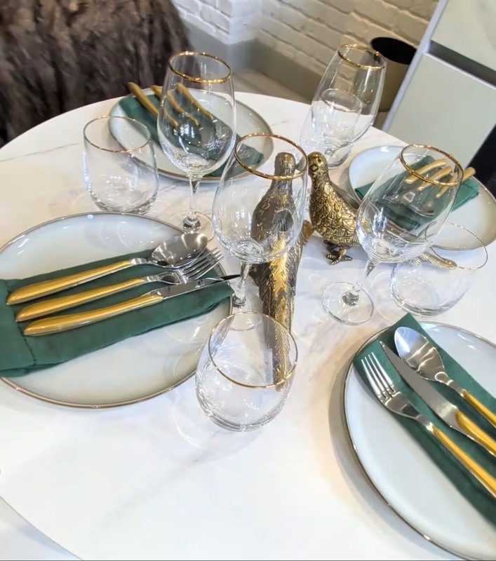 Formal dining table set with white plates, wine glasses, gold cutlery and green napkins