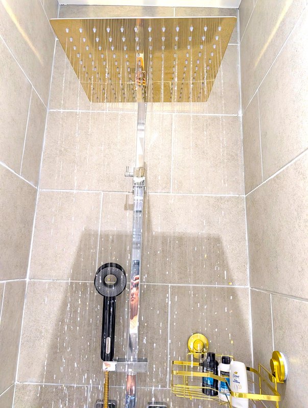 Modern bathroom with rainfall showerhead, tiled walls, and cleaning supplies on floor