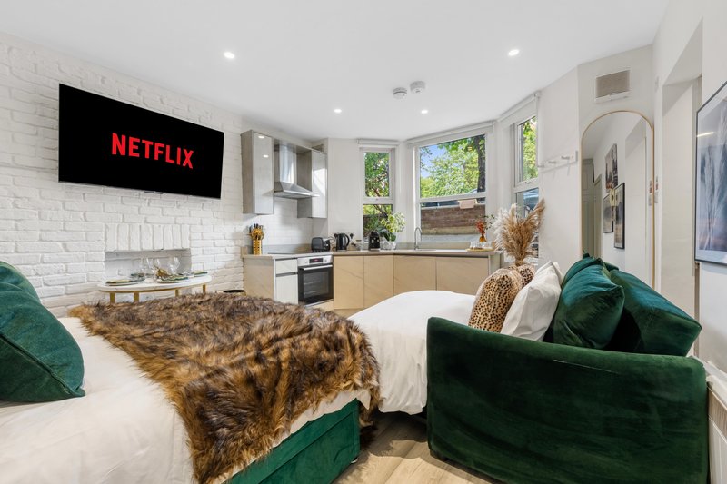 Modern open-plan studio with double bed, green velvet sofa, kitchenette and white brick walls