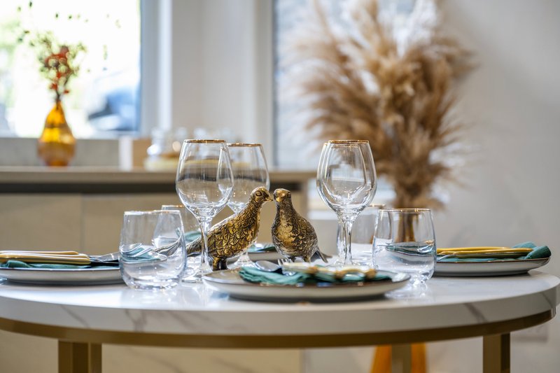 Round dining table set with glasses, plates, and gold decorative bird figurines