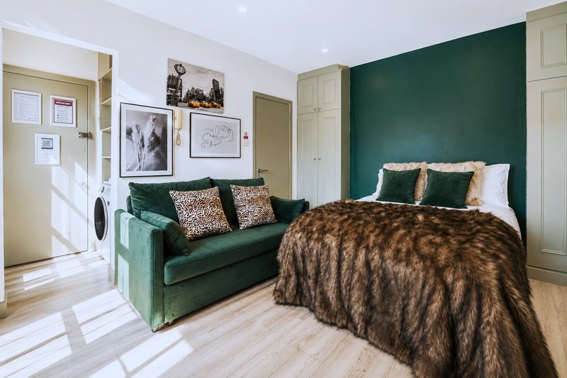 Spacious bedroom with green accent wall, double bed, green velvet sofa, and en-suite bathroom visible