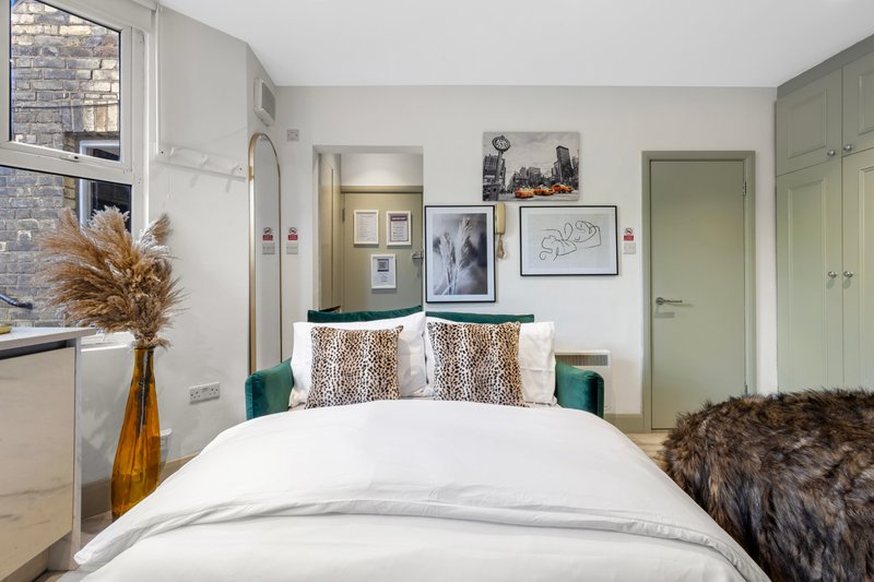 Modern bedroom with white bed, decorative cushions, pampas grass in vase, and green wardrobe doors