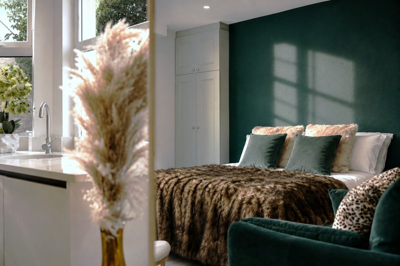 Modern bedroom with dark green accent wall, double bed with patterned bedding, and decorative pampas grass arrangement