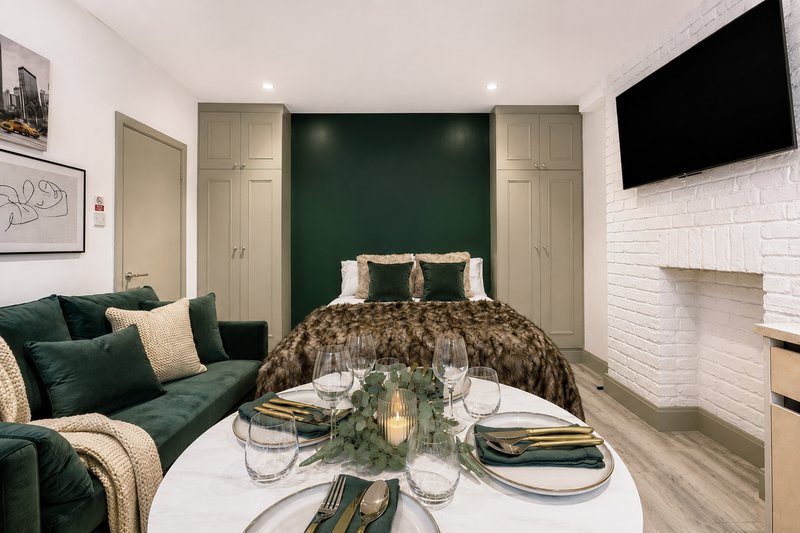 Modern bedroom with green accent wall, double bed, sofa seating area and dining table setup