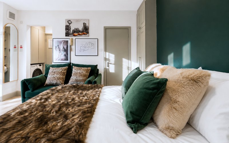 Modern bedroom with double bed, green velvet armchair, and forest green accent wall
