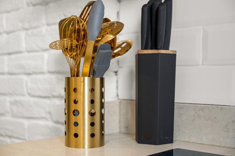 Kitchen counter with gold utensil holder containing cooking utensils and black knife block