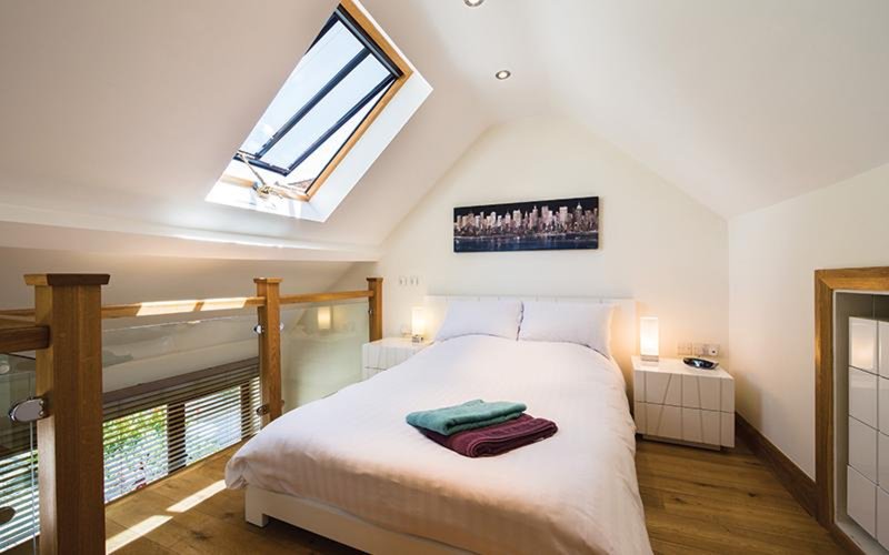Bright attic bedroom with skylight, wooden bed frame, white bedding and wooden flooring