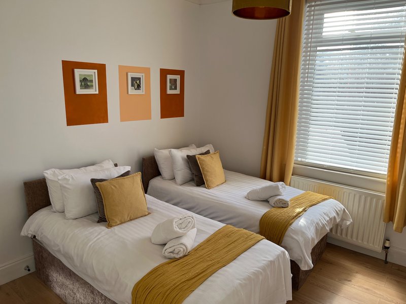 Bright bedroom with two single beds, gold and white bedding, wooden floor and framed wall art