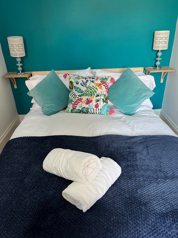 Bedroom with teal accent wall, double bed, decorative cushions and rolled towels