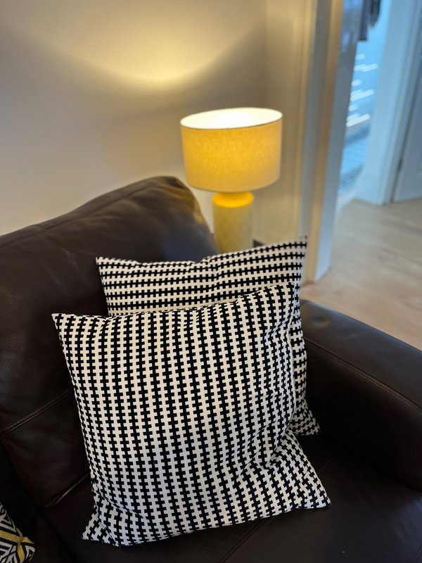 Black leather sofa with patterned cushions, yellow table lamp, and window with blue curtains