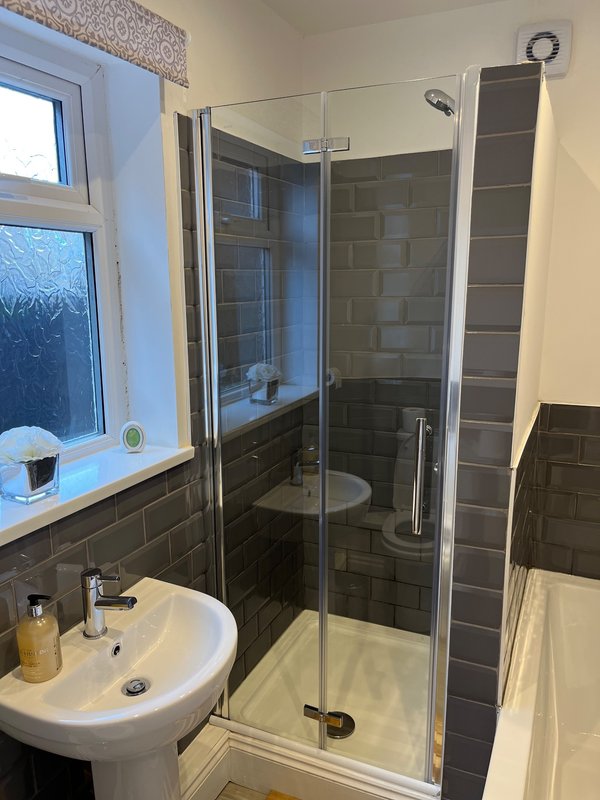 Modern bathroom with walk-in shower, pedestal sink, window and dark tile walls