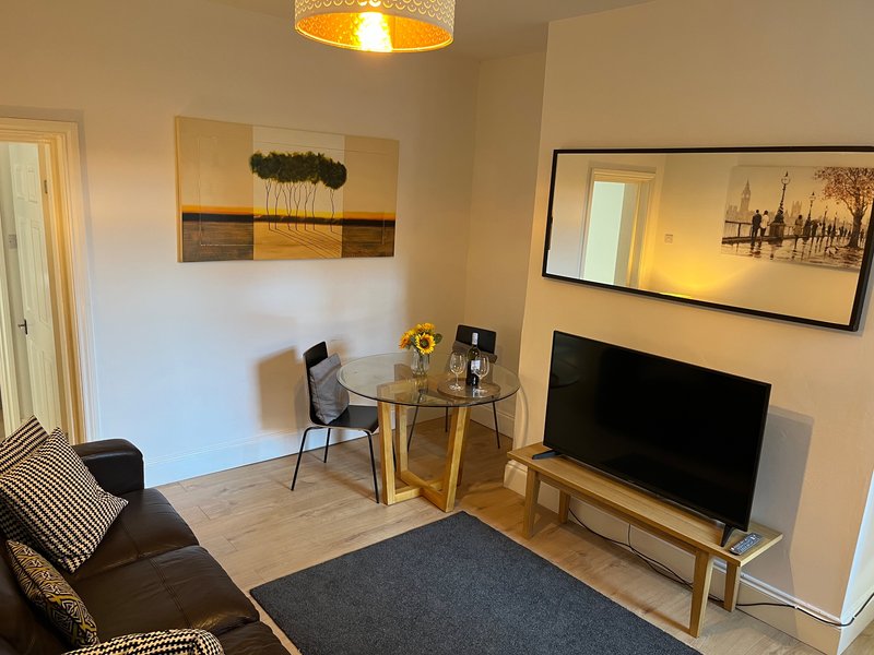 Modern living room with TV, small dining table, black sofa and framed wall art