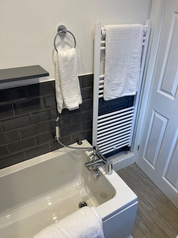 Modern bathroom with bathtub, towel rails, black tile wall, and white towels