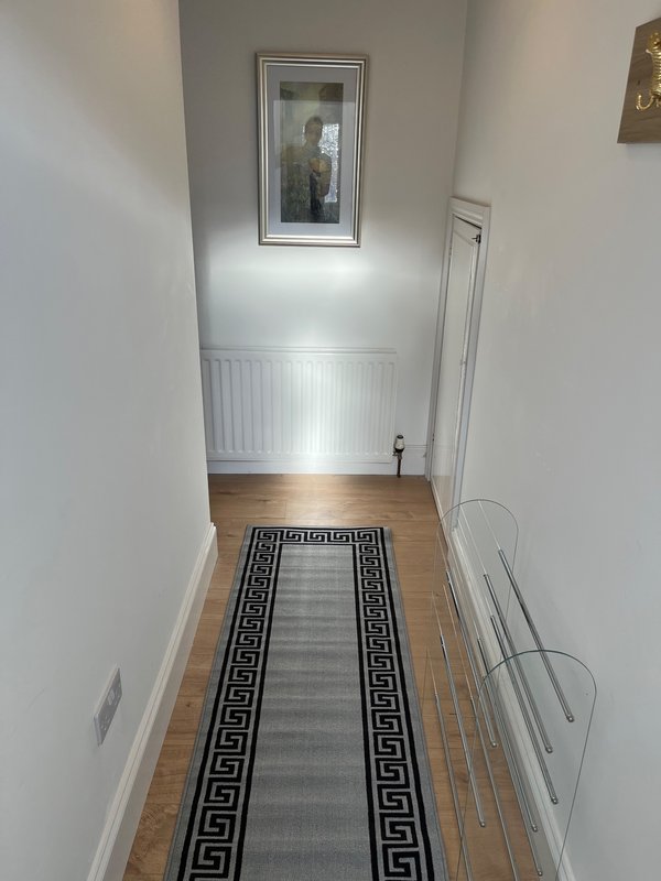 Narrow hallway with wooden flooring, white walls, radiator and framed mirror on wall