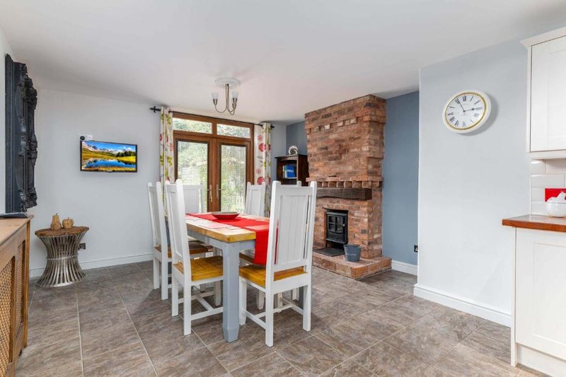 Open-plan dining and kitchen area with wooden table, brick fireplace, and glass doors