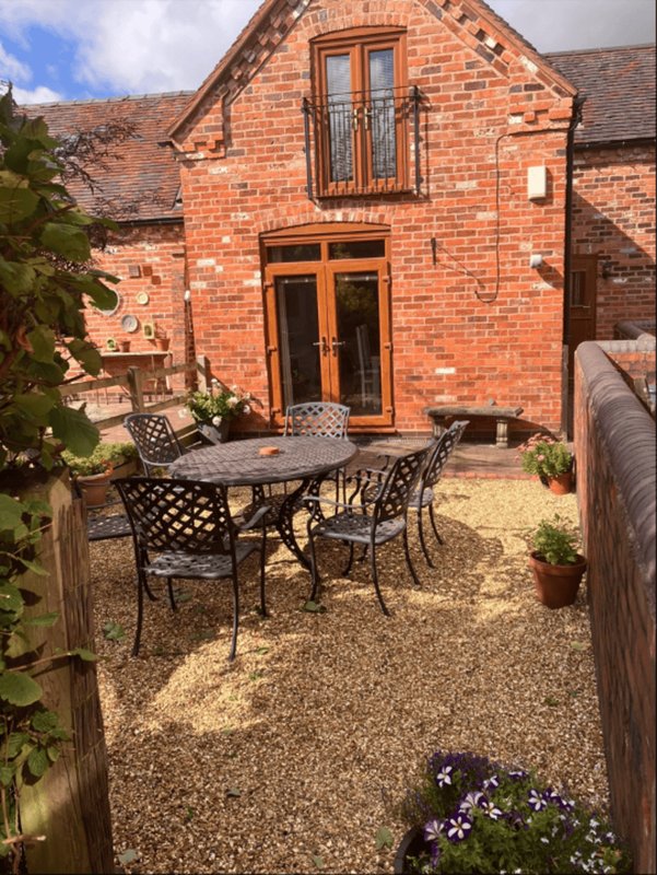 Brick cottage exterior with patio seating area, garden plants and gravel courtyard