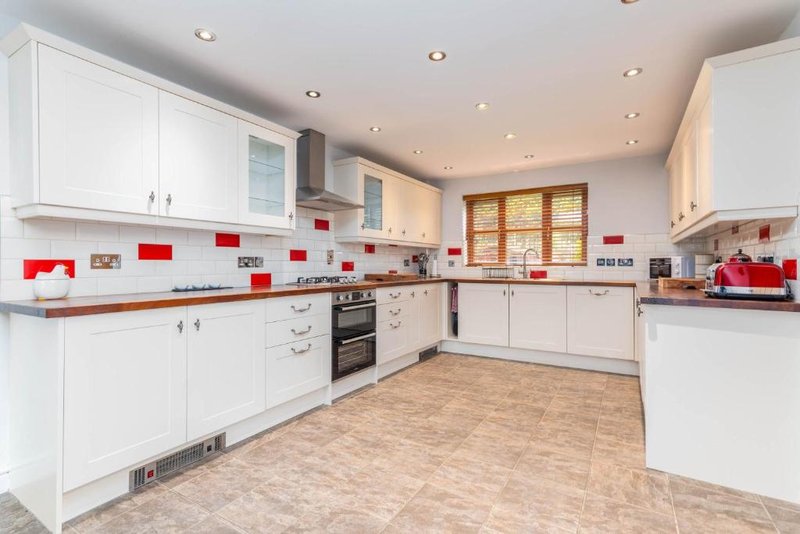 Modern kitchen with white cabinetry, red tile backsplash, and wooden floor