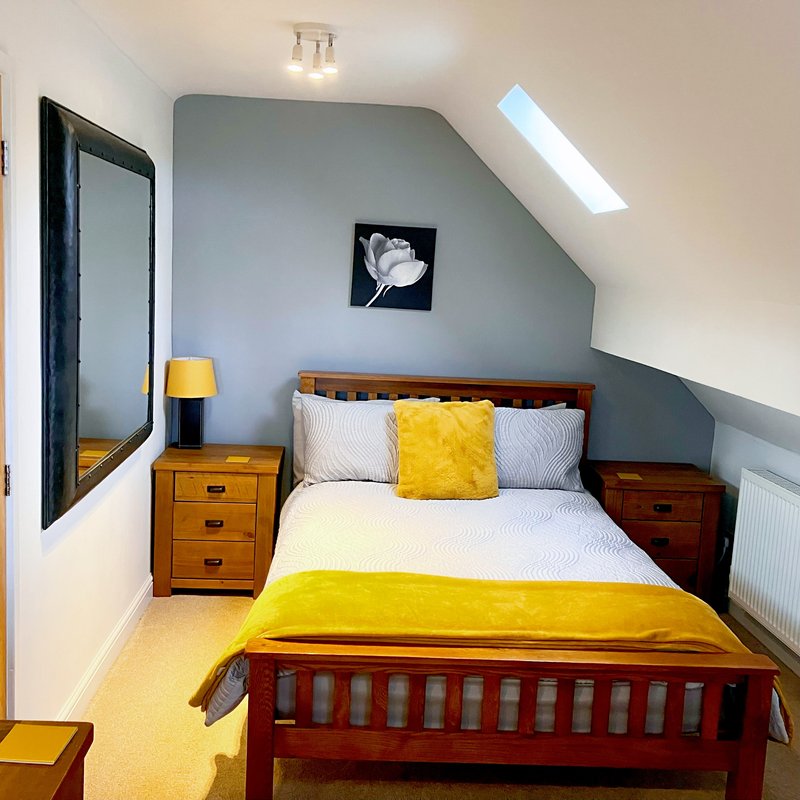 twin bedroom with wooden bed frame, yellow bedding, wooden nightstands, and sloped ceiling with skylight