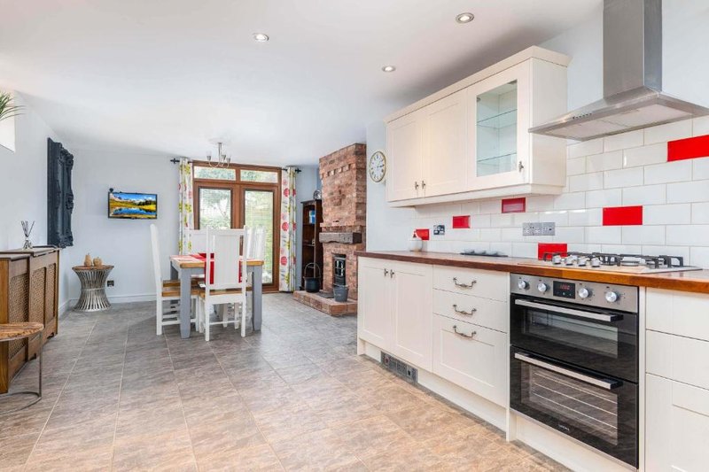 Open-plan kitchen and dining area with white cabinetry, red tile accents, and wooden dining table