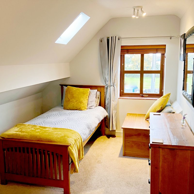 Bright twin bedroom with single wooden bed, yellow bedding, desk, and skylight window