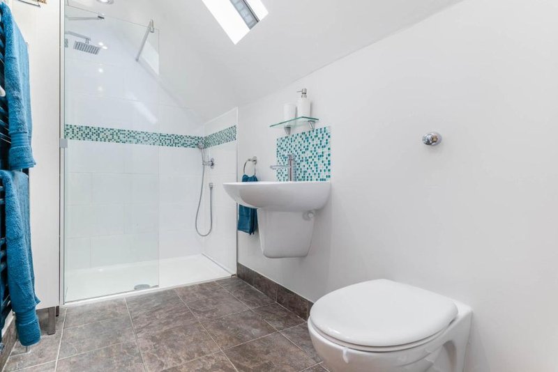 Modern bathroom with shower enclosure, wall-mounted sink, toilet, and teal tile accents