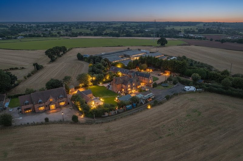 Aerial dusk view of large country estate with illuminated buildings surrounded by farmland