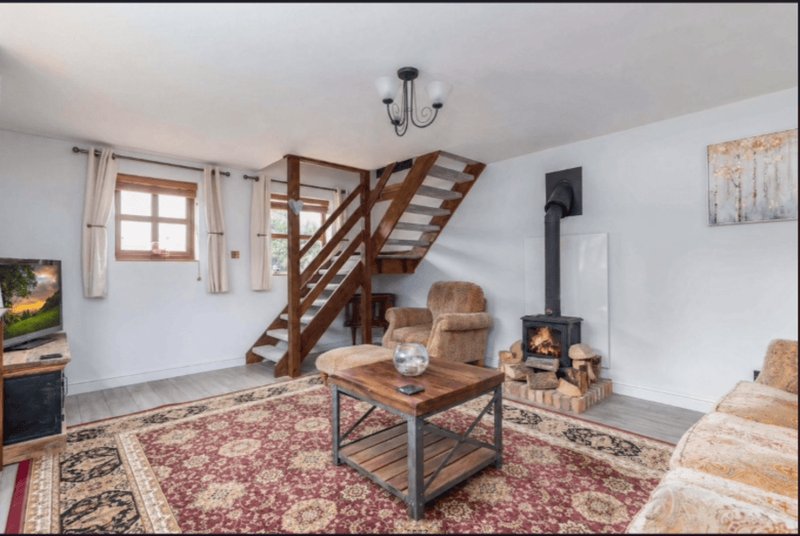 Open-plan living room with wooden staircase, fireplace, upholstered chairs and coffee table