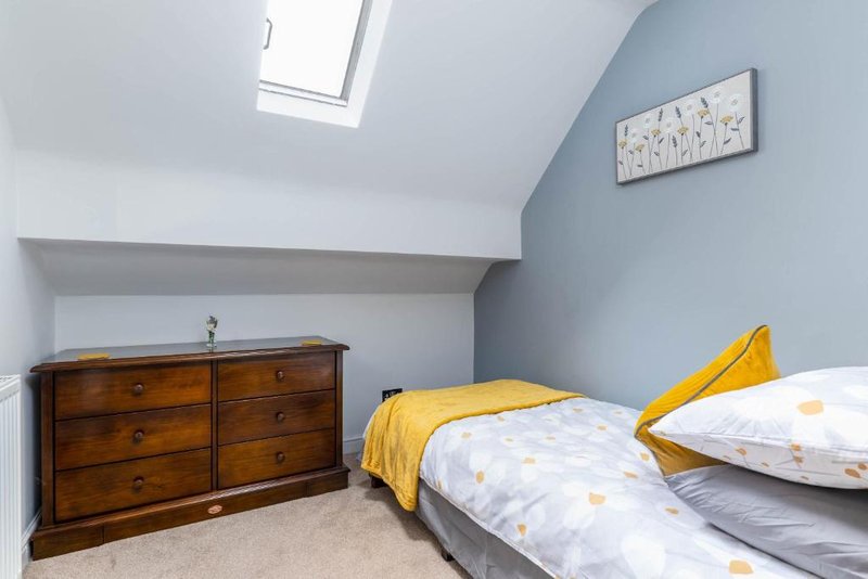 Bright single bedroom, wooden chest of drawers, skylight window and blue-painted walls.