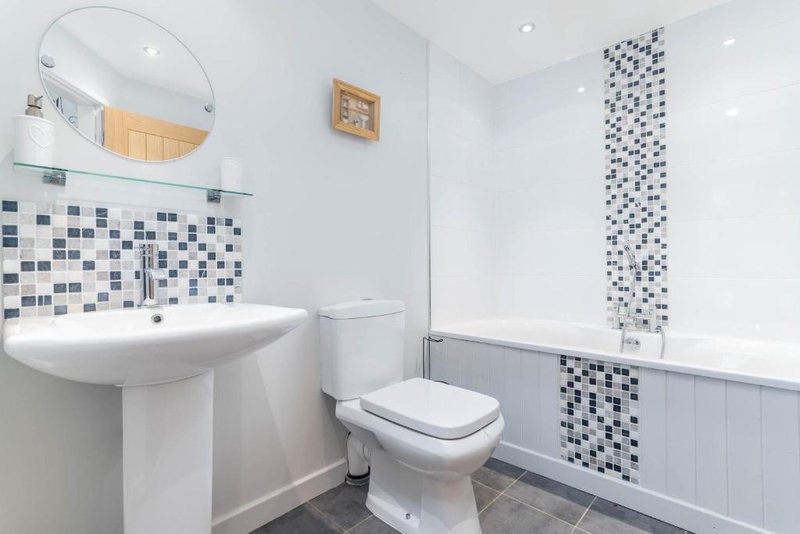 Clean modern bathroom with pedestal sink, toilet, mosaic tile accents and round mirror