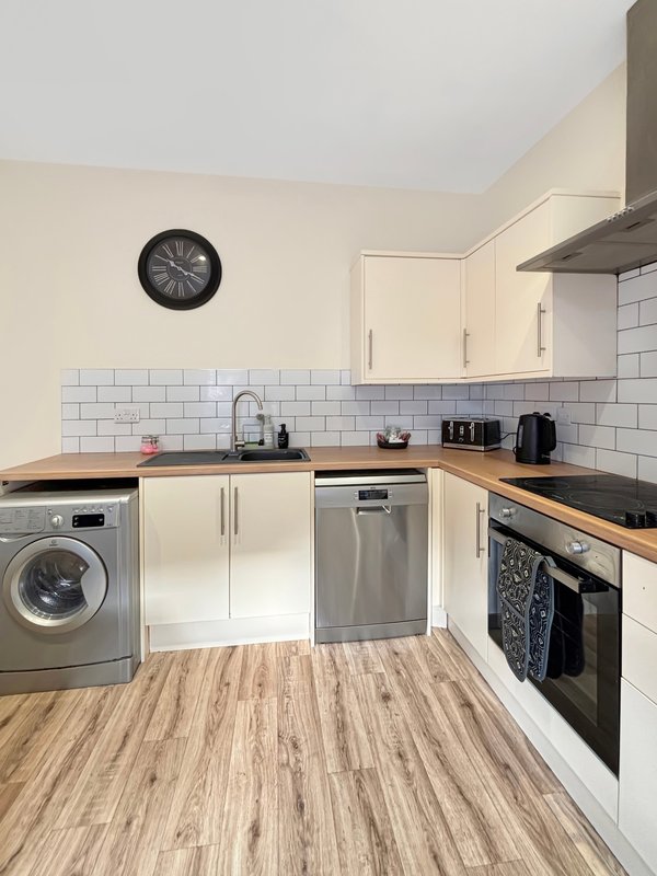 Modern kitchen with cream units, wooden countertops, stainless steel appliances, and tiled splashback
