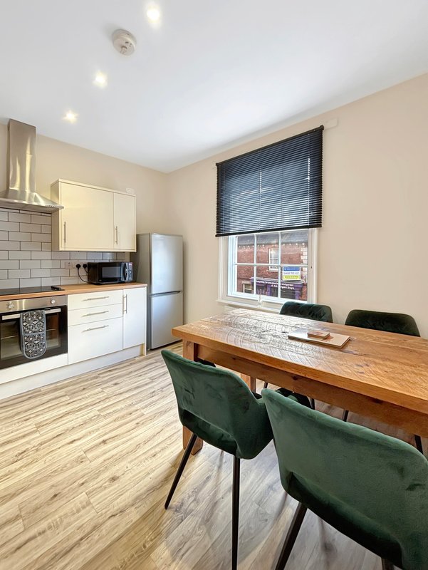 Open-plan kitchen and dining area with white cabinetry, wooden table, and green chairs