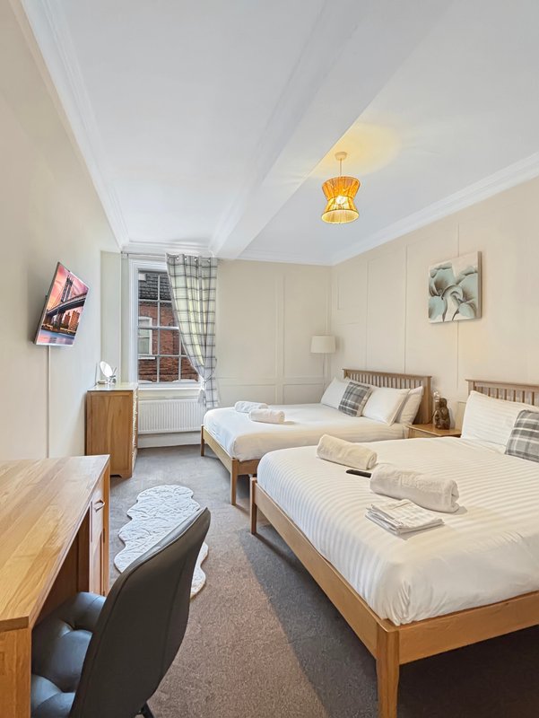 Bright twin bedroom with two single beds, wooden furniture, window with checked curtains and pendant lamp