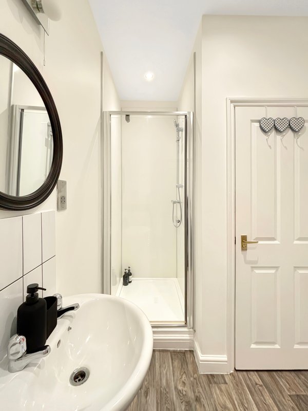 Clean bathroom with round mirror, white sink, shower enclosure and wooden flooring
