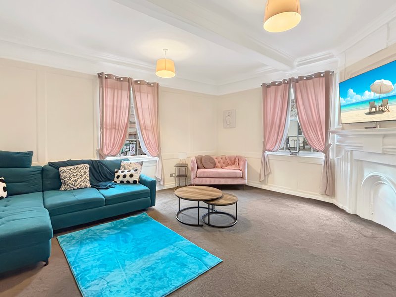 Spacious living room with teal sofa, pink armchair, fireplace and large windows