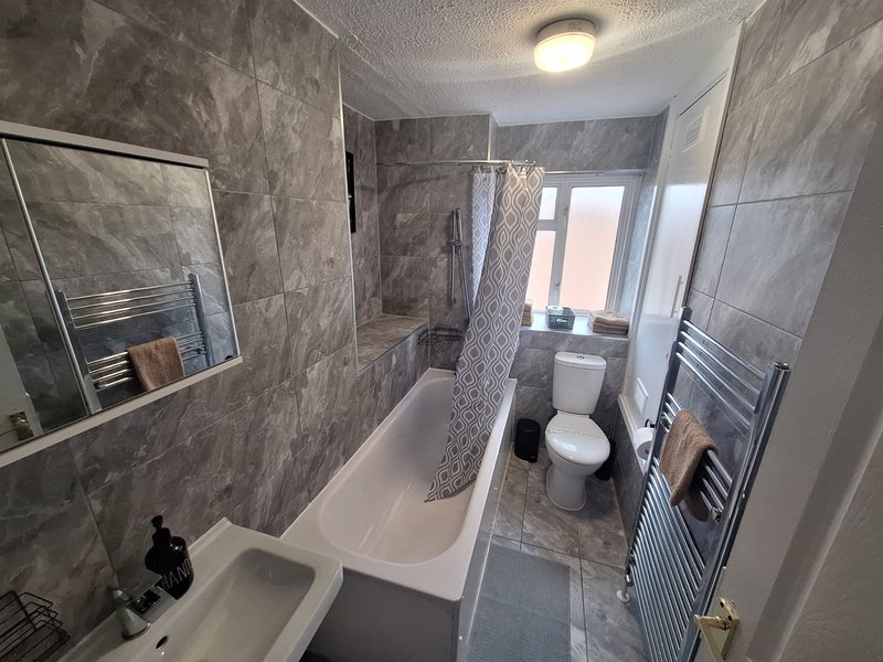 Modern bathroom with gray tile walls, white bathtub, toilet, and heated towel rails